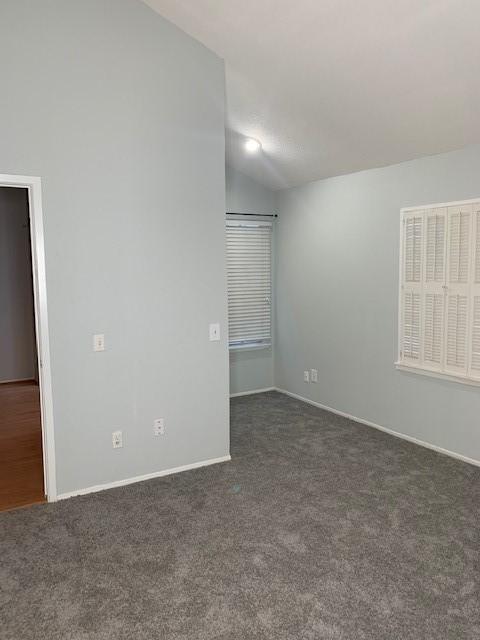 spare room with lofted ceiling, dark colored carpet, and baseboards