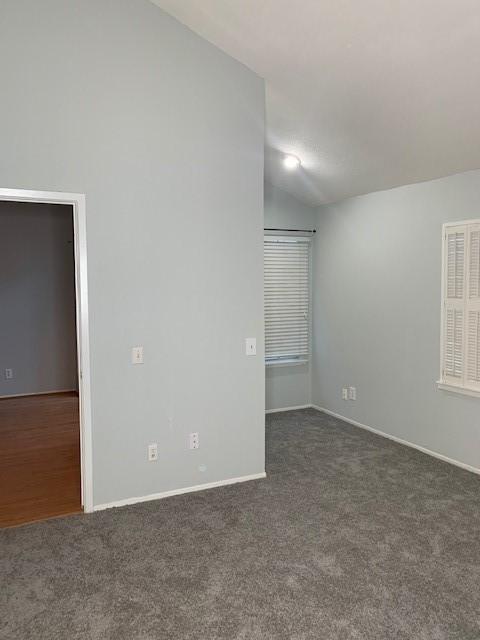 empty room with carpet floors, vaulted ceiling, and baseboards
