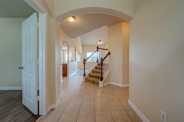 hallway featuring arched walkways, baseboards, light tile patterned floors, stairway, and vaulted ceiling