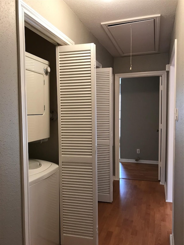 laundry area with estacked washer and dryer, attic access, and wood finished floors