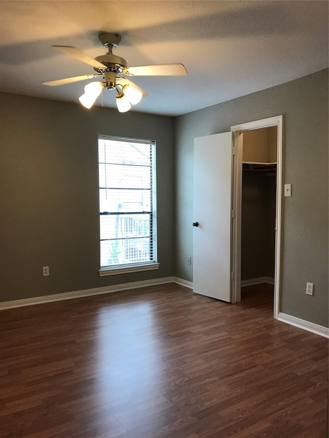 unfurnished bedroom with dark wood-style floors, baseboards, a closet, and a spacious closet