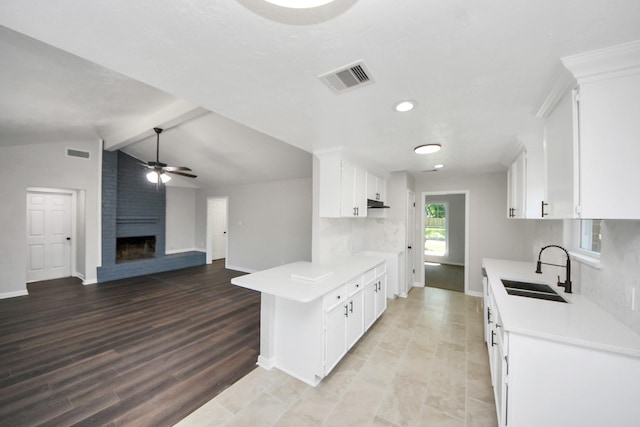 kitchen featuring a sink, light countertops, a large fireplace, ceiling fan, and baseboards