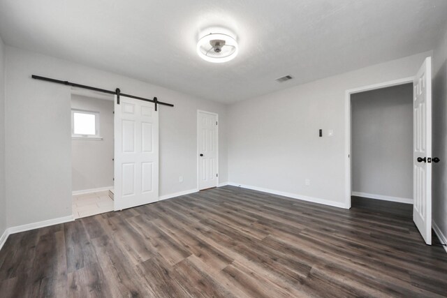 unfurnished bedroom featuring a barn door, baseboards, and dark wood-style floors