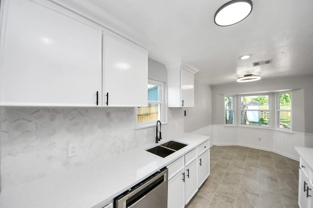kitchen with a sink, stainless steel dishwasher, backsplash, light countertops, and white cabinets