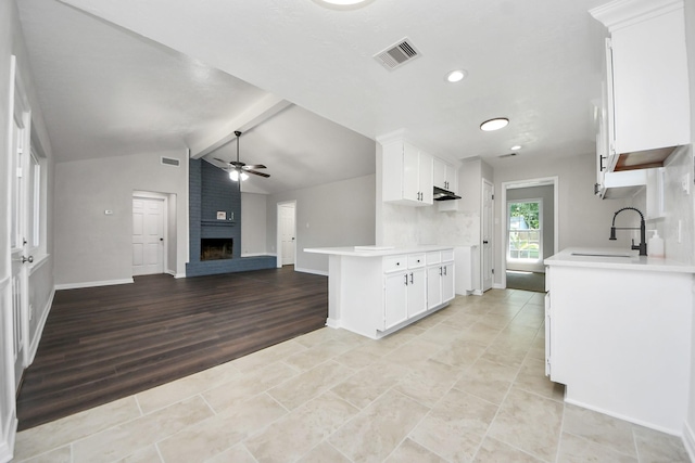 kitchen featuring a sink, ceiling fan, a fireplace, light countertops, and white cabinets