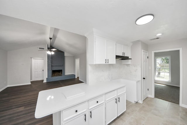 kitchen featuring under cabinet range hood, ceiling fan, baseboards, white cabinetry, and a brick fireplace