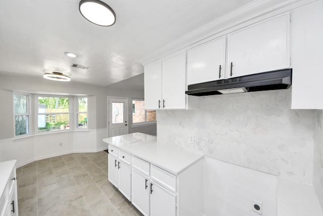 kitchen with under cabinet range hood, light countertops, white cabinetry, and a wainscoted wall