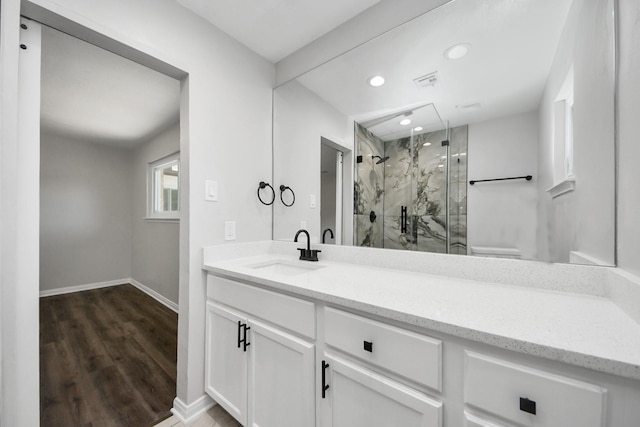 bathroom featuring a marble finish shower, baseboards, wood finished floors, vanity, and recessed lighting