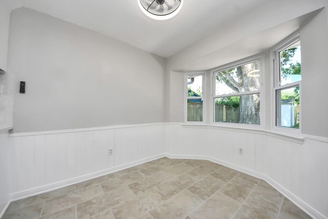 empty room with lofted ceiling and a wainscoted wall