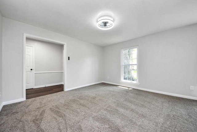 spare room featuring dark carpet and baseboards