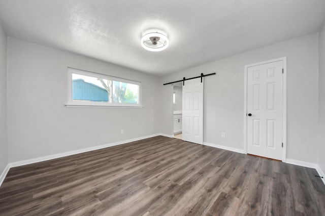unfurnished bedroom with a barn door, dark wood-style flooring, and baseboards