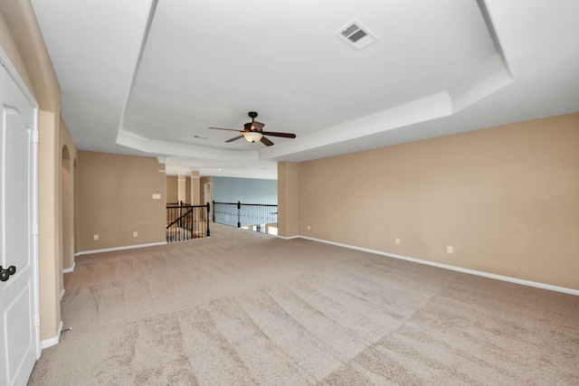 carpeted empty room with a tray ceiling, ceiling fan, and baseboards