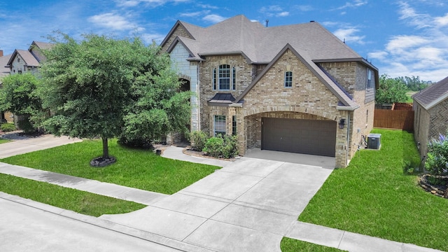 french provincial home with a garage, concrete driveway, a shingled roof, central air condition unit, and brick siding