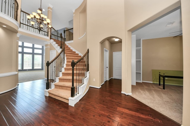 foyer entrance with a towering ceiling, hardwood / wood-style floors, stairs, baseboards, and arched walkways
