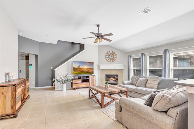 living room with lofted ceiling, ceiling fan, a tiled fireplace, light tile patterned floors, and baseboards