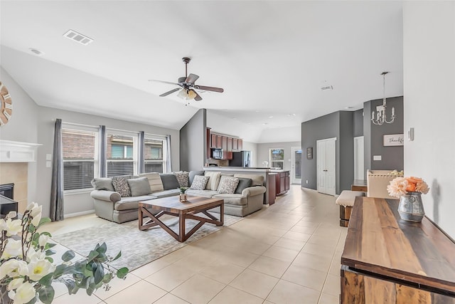 living area featuring a ceiling fan, light tile patterned floors, a chandelier, vaulted ceiling, and a tile fireplace
