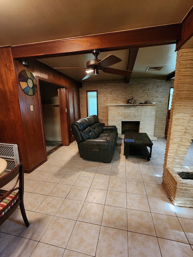 living room featuring ceiling fan, light tile patterned floors, wood walls, and a fireplace with raised hearth