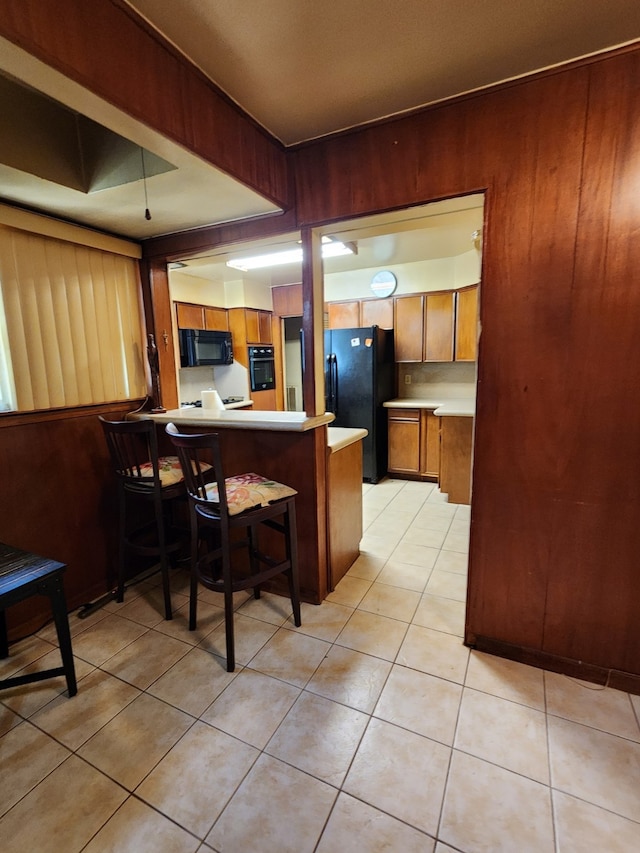 kitchen with black appliances, brown cabinetry, light countertops, a peninsula, and wooden walls