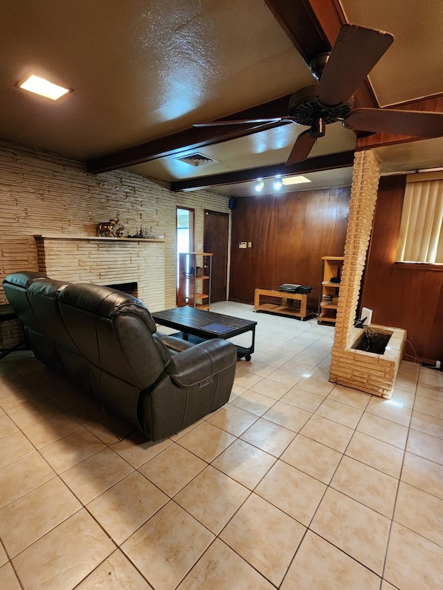living room with wood walls, beam ceiling, ceiling fan, light tile patterned floors, and a brick fireplace