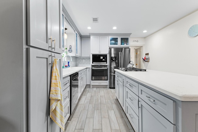 2120 73rd St, Galveston, TX 77551 - kitchen featuring black appliances, tasteful backsplash, a sink, a center island, and glass insert cabinets