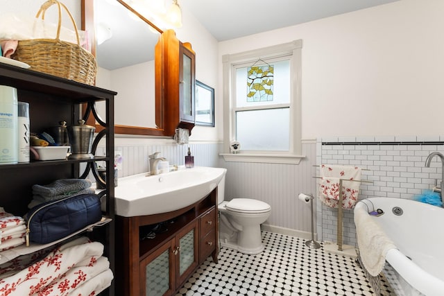2120 73rd St, Galveston, TX 77551 - bathroom with wainscoting, toilet, vanity, a soaking tub, and baseboards
