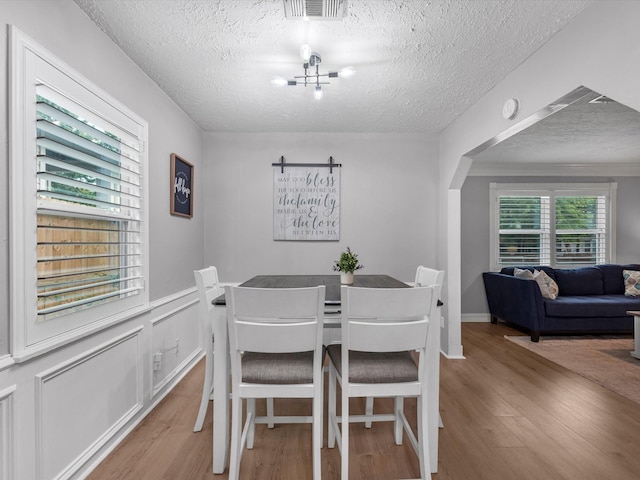 dining space with wood finished floors, a textured ceiling, a chandelier, and arched walkways