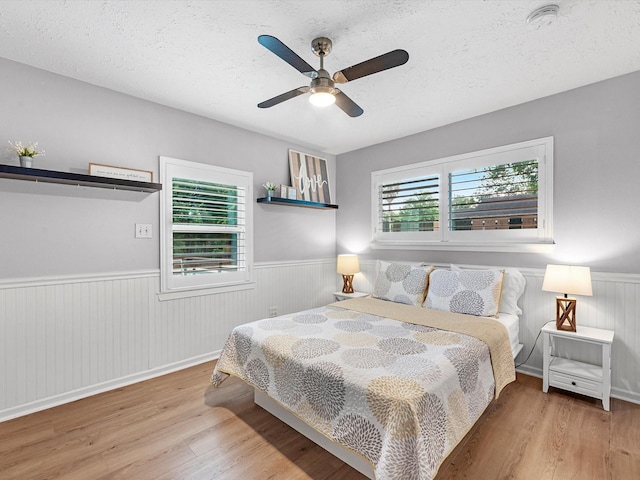 bedroom featuring wainscoting, wood finished floors, a textured ceiling, and a ceiling fan