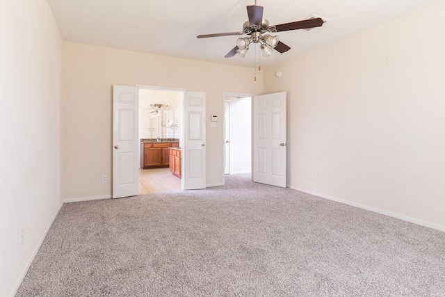 unfurnished bedroom featuring light carpet, baseboards, ensuite bathroom, and a ceiling fan