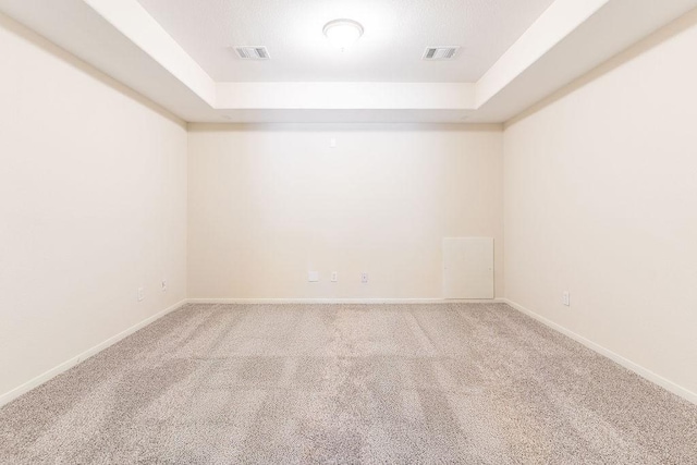 carpeted spare room with a tray ceiling and baseboards