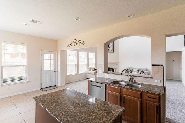 kitchen with open floor plan, a sink, arched walkways, a fireplace, and dark stone countertops