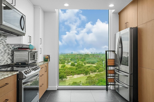 kitchen featuring appliances with stainless steel finishes, dark tile patterned flooring, light stone counters, decorative backsplash, and healthy amount of natural light