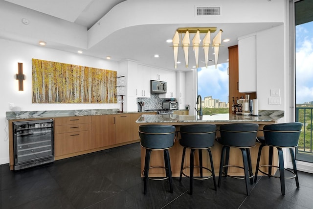 kitchen featuring stainless steel microwave, beverage cooler, a peninsula, a kitchen bar, and tasteful backsplash