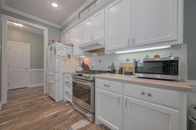 8946 Catamaran Way, Montgomery, TX 77316 - kitchen featuring stainless steel appliances, under cabinet range hood, crown molding, white cabinetry, and light wood finished floors