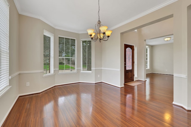 empty room featuring a chandelier, wood finished floors, healthy amount of natural light, and ornamental molding