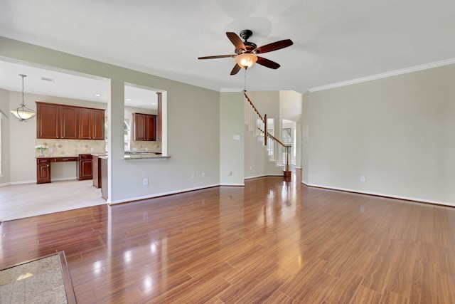 unfurnished living room with crown molding, ceiling fan, stairway, wood finished floors, and baseboards
