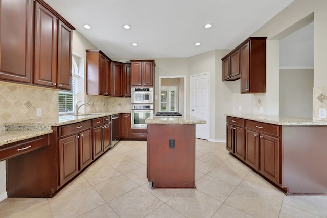 kitchen with appliances with stainless steel finishes, backsplash, a sink, a kitchen island, and light stone counters