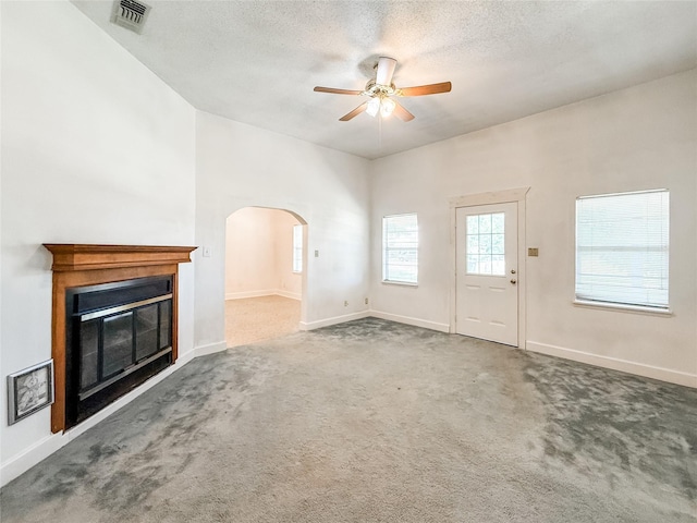 102 Besch Wilburn Ln, Glidden, TX 78943 - unfurnished living room with a ceiling fan, arched walkways, a glass covered fireplace, carpet floors, and a textured ceiling