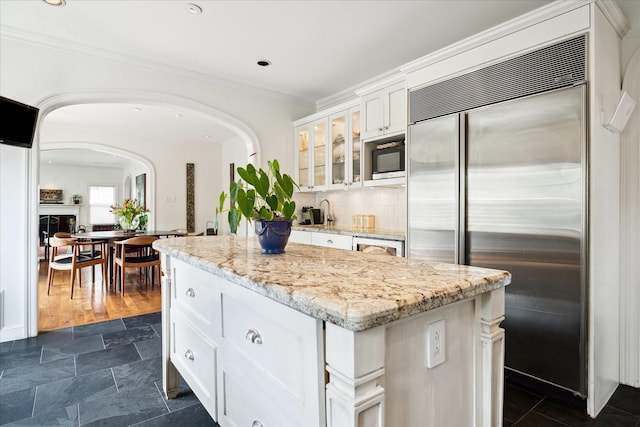 1755 Kipling St, Houston, TX 77098 - kitchen featuring built in appliances, a center island, glass insert cabinets, white cabinets, and arched walkways