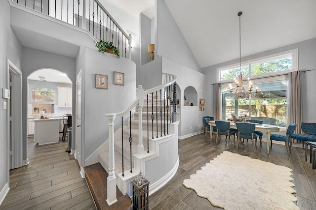 stairs with arched walkways, high vaulted ceiling, a chandelier, and wood finished floors