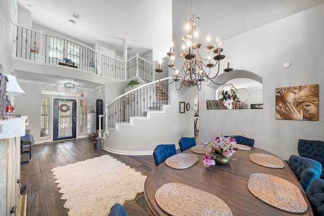 dining room with a towering ceiling, wood finished floors, stairway, a chandelier, and arched walkways