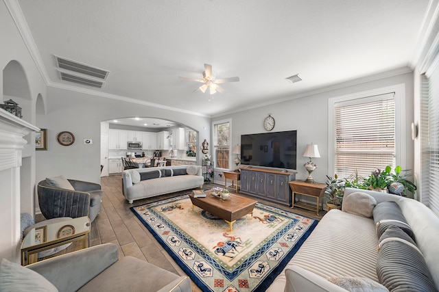 living room featuring arched walkways, ornamental molding, ceiling fan, and light wood-type flooring