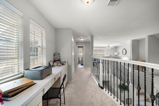 corridor with an office area, light carpet, and baseboards