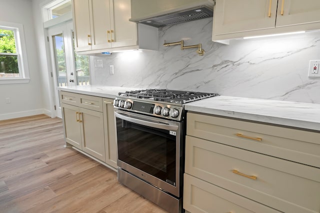 3224 Omega St, Houston, TX 77022 - kitchen featuring stainless steel gas range, ventilation hood, light wood-style floors, backsplash, and baseboards