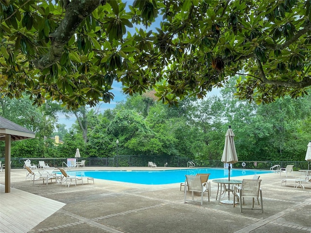 community pool featuring fence, view of wooded area, and a patio area