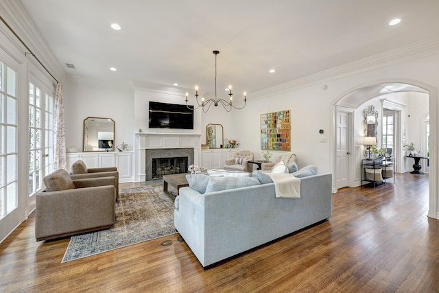 living area featuring arched walkways, plenty of natural light, a fireplace, crown molding, and wood finished floors