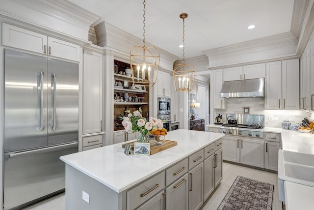 kitchen with built in appliances, under cabinet range hood, decorative backsplash, a chandelier, and gray cabinetry