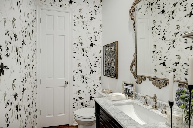 bathroom featuring toilet, vanity, and wallpapered walls