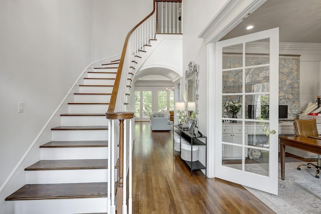 stairs with french doors, wood finished floors, a towering ceiling, ornamental molding, and recessed lighting
