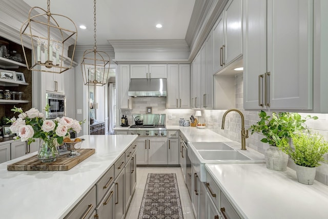 kitchen with under cabinet range hood, light countertops, stainless steel microwave, tasteful backsplash, and ornamental molding