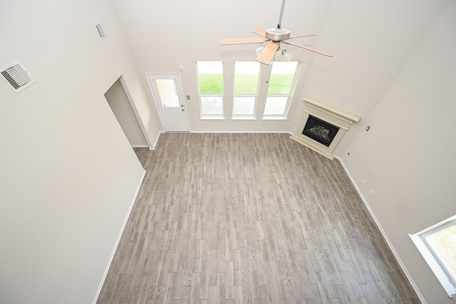 108 Shallow Creek Dr, Waller, TX 77445 - unfurnished living room with a ceiling fan, a glass covered fireplace, wood finished floors, baseboards, and a high ceiling